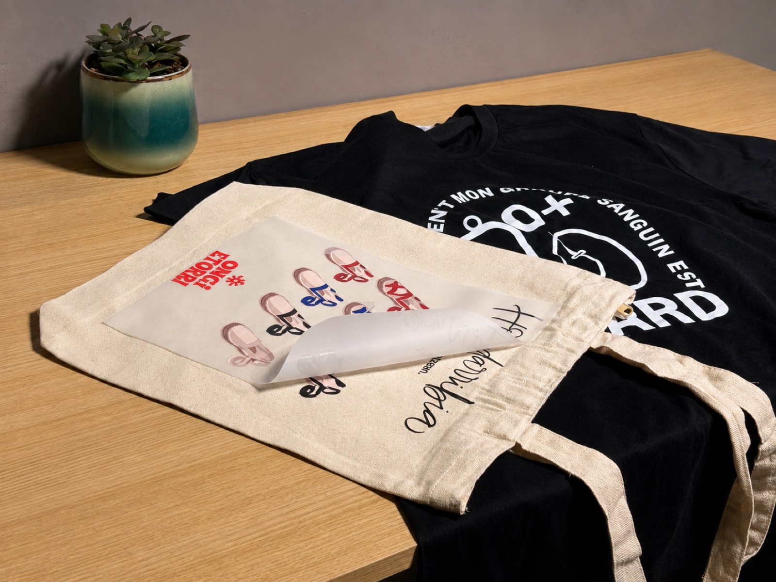 Film DTF despegándose de una bolsa de algodón recién planchada, junto a una camiseta negra personalizada
